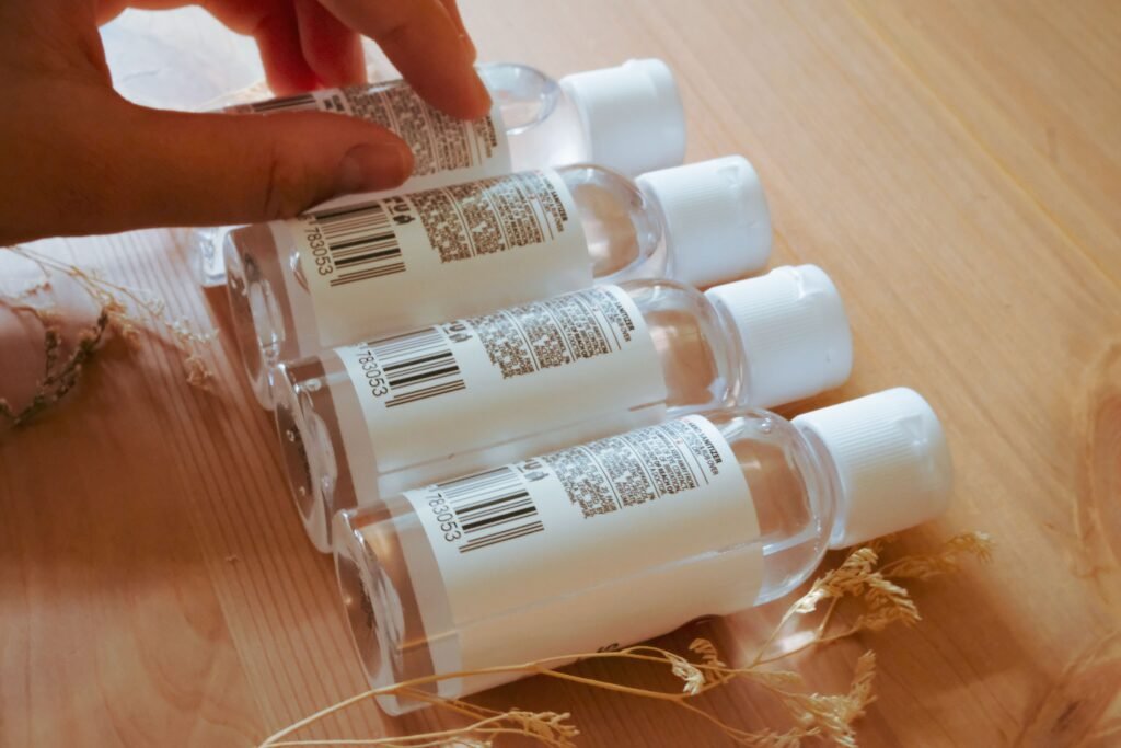 Close-up of a hand organizing clear sanitizer bottles on a wooden surface.